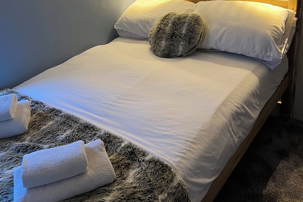 A neatly made bed with white linens, a fluffy throw blanket, and two towels folded at the foot of the bed.