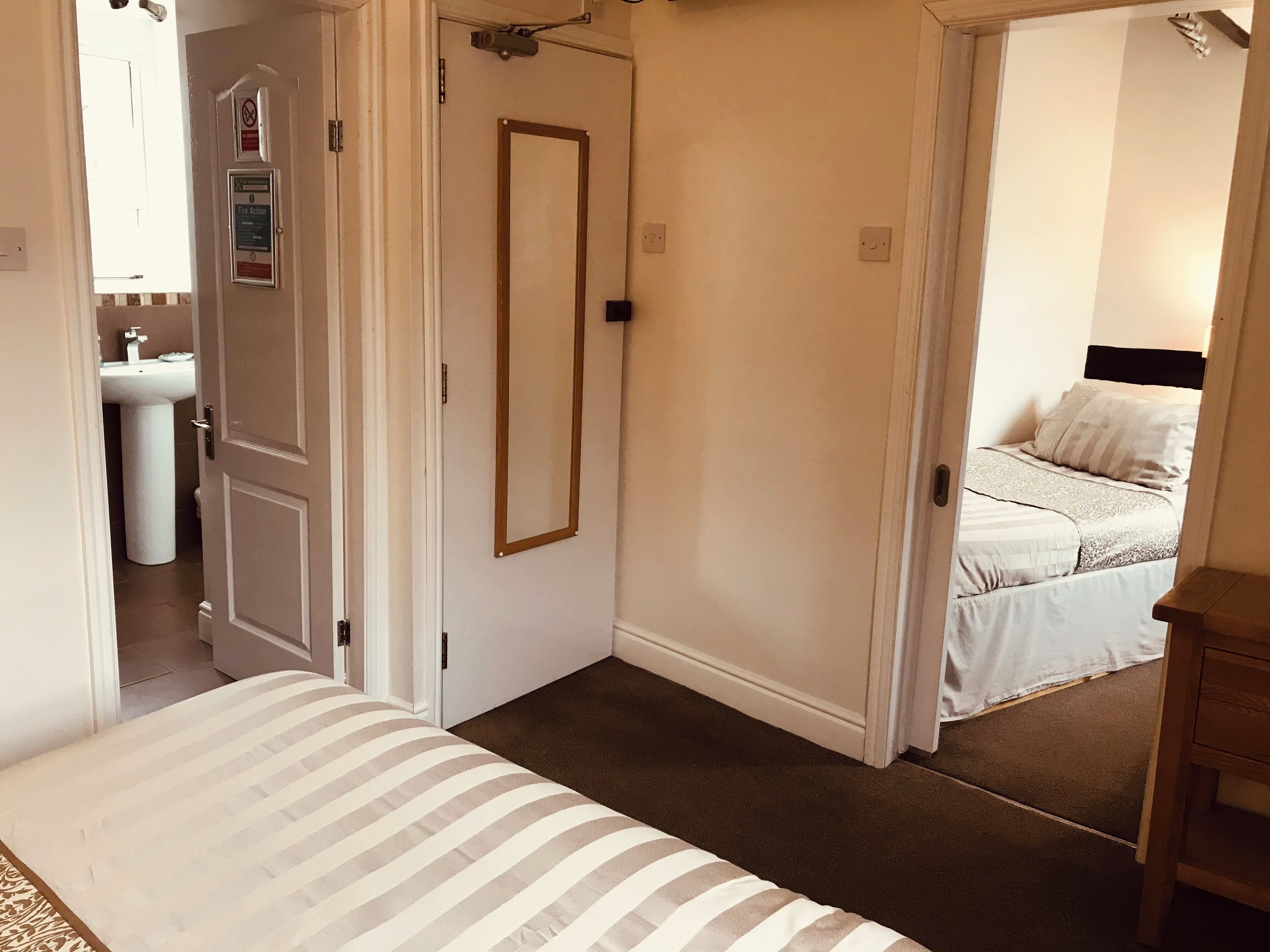 A bedroom with a bed, a bedside table, a mirror, and a door leading to a bathroom.