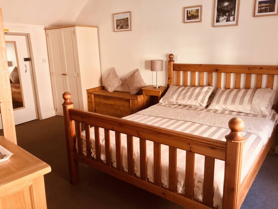 A bedroom with a wooden bed, a wooden nightstand, a wardrobe, and a door leading to another room.