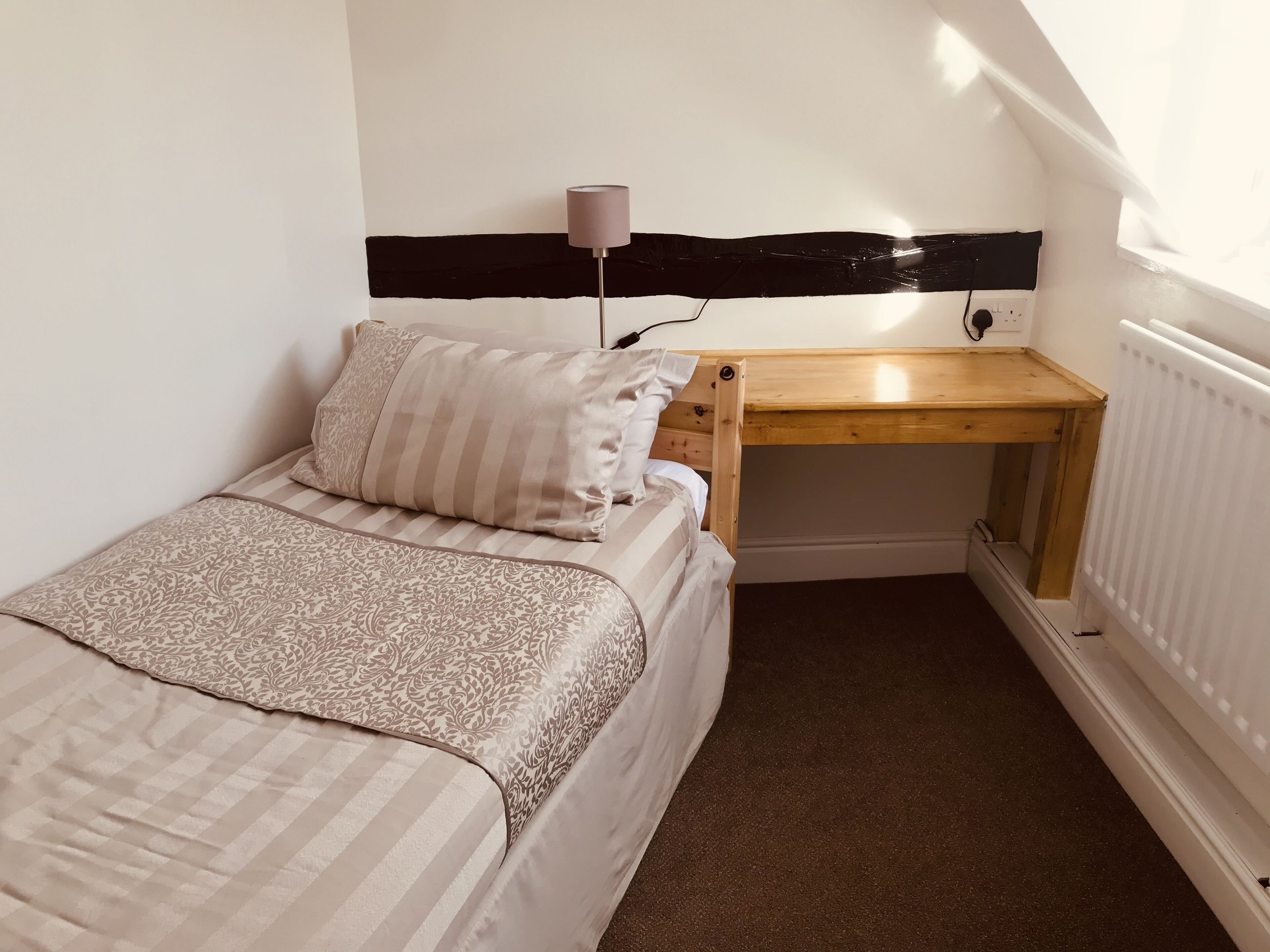 A small, cozy bedroom with a bed, a bedside table, a lamp, and a radiator.