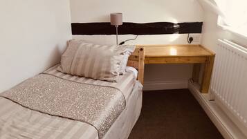 A small, cozy bedroom with a bed, a bedside table, a lamp, and a radiator.