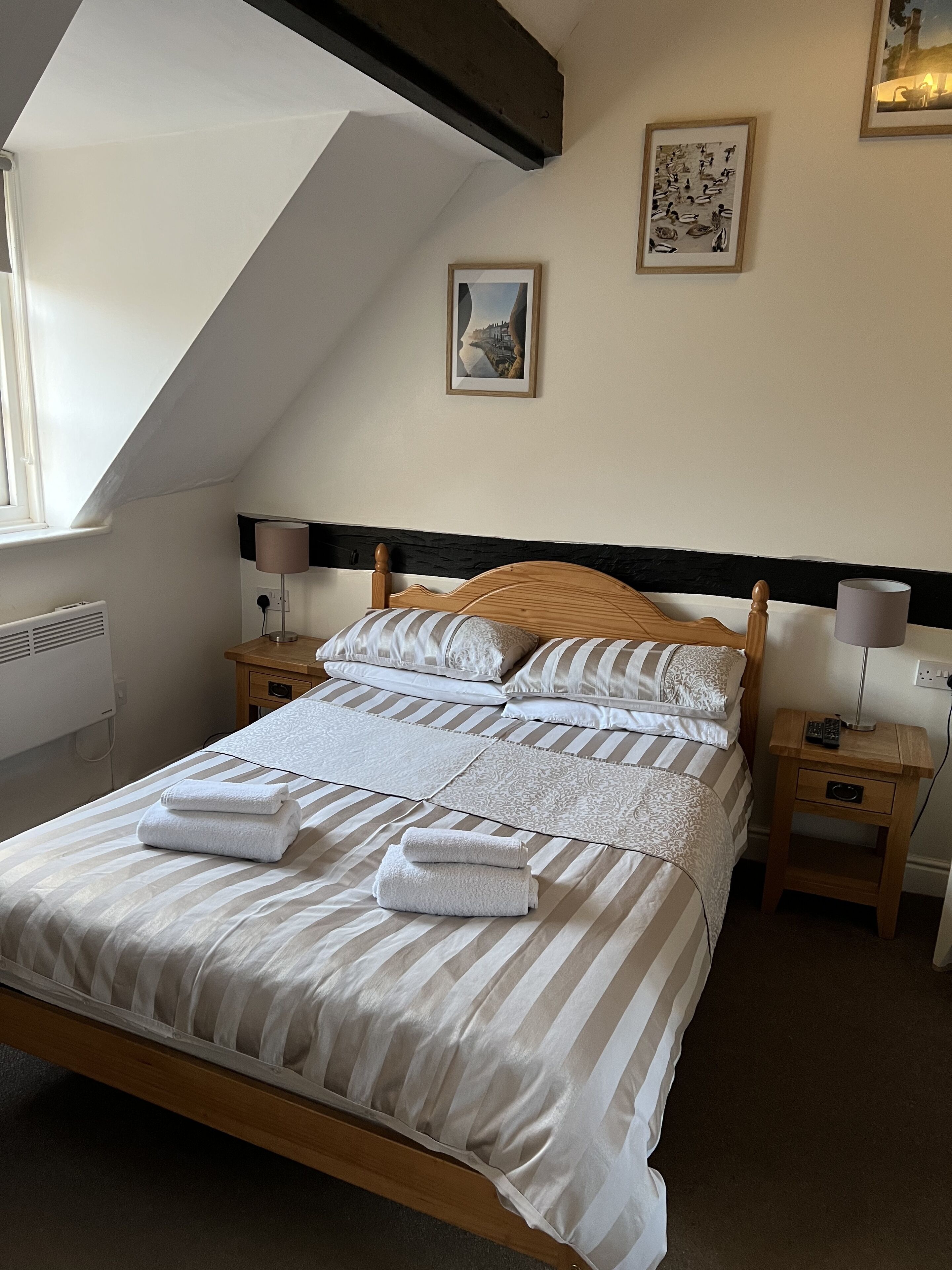 A neatly made bed with striped bedding and folded towels, a wooden headboard, bedside lamps, and two framed pictures on the wall.