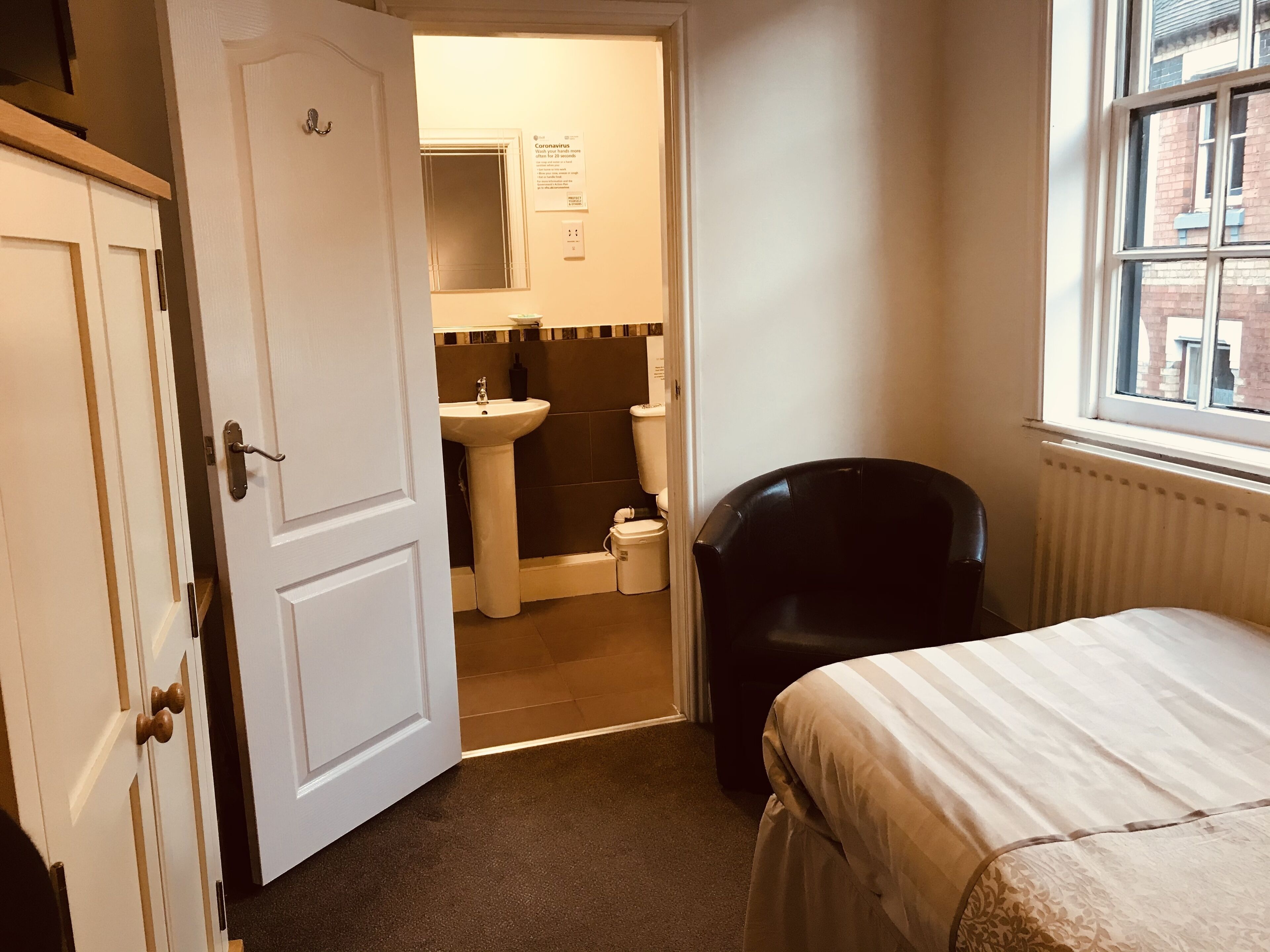 Ein Schlafzimmer mit Bett, Stuhl, Fenster und einem durchgegangenen Tür sichtbarem Badezimmer.