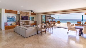 A spacious living area with a large sofa, armchairs, and a dining set. A large window offers a view of the ocean. - Stunning 6 bedroom home on best sand beach, 45’ pool/jacuzzi, Bar, BBQ, fire-pit (Bahia de Los Frailes)