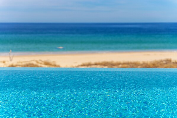On voit clairement une piscine, une plage de sable et l’océan en arrière-plan.