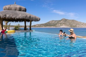 Une piscine d’eau cristalline, bordée d’une structure au toit de chaume, le tout niché au cœur d’un paysage montagneux.