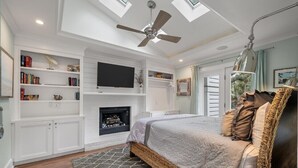Une chambre à coucher avec un lit, une cheminée, un ventilateur de plafond et des étagères intégrées.
