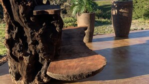 A rustic outdoor seating area with a large wooden sculpture, a palm plant, and a potted tree. - California Dreamin' Upscale Architectural marvel / Horizon ocean view on 3 acres (Arroyo Grande)