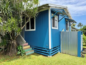 A small, single-story house with a blue exterior, a porch with steps, and a fenced yard.