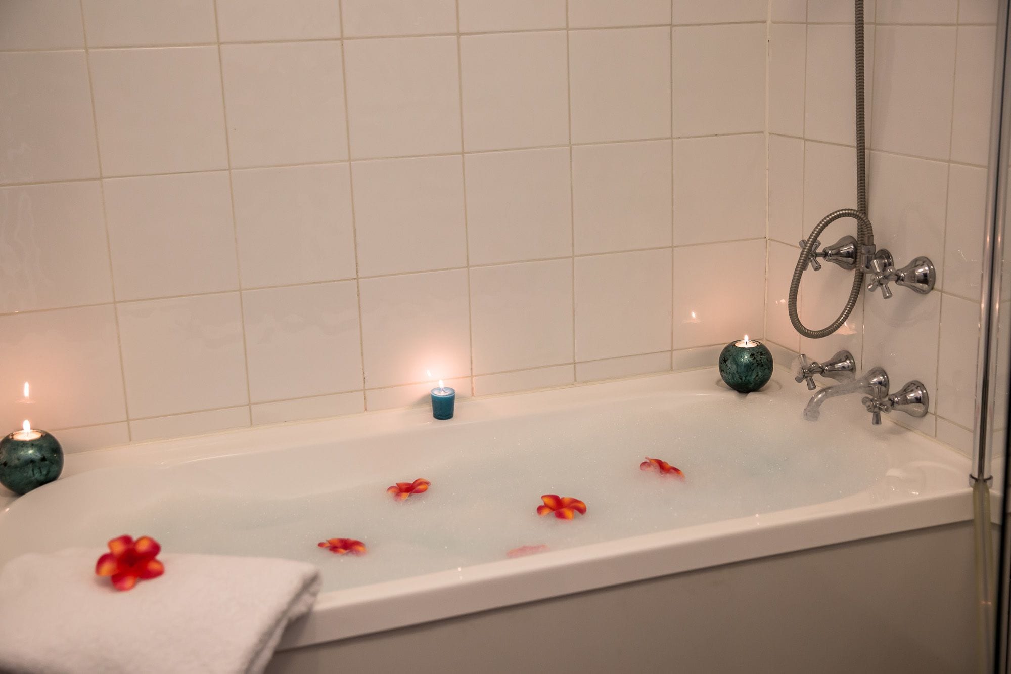 Una bañera con un vaso de agua, una vela y pétalos de flores.