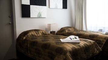 Quarto de hotel com duas camas, cada uma com colcha estampada, mesa de cabeceira com abajur e uma obra de arte na parede.