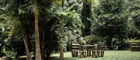 A garden with a brick pathway leading to a wooden table and chairs set up for dining.