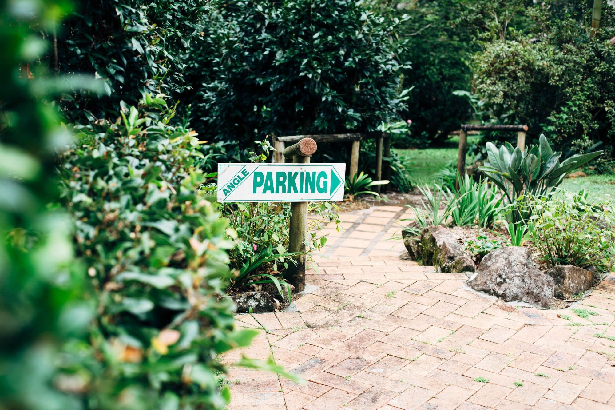 A pathway leading to a parking area, surrounded by lush greenery and a brick walkway.