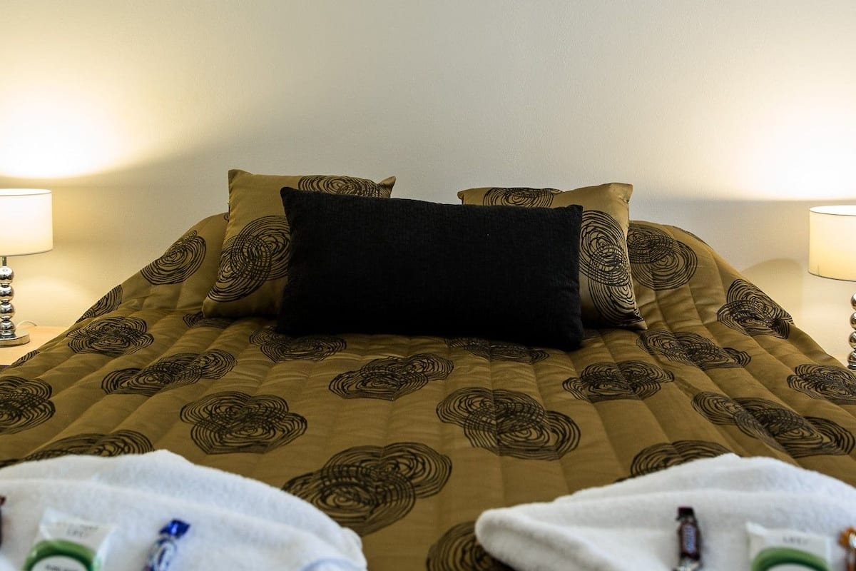 A neatly made bed with a patterned bedspread, two bedside lamps, and towels on the bed.
