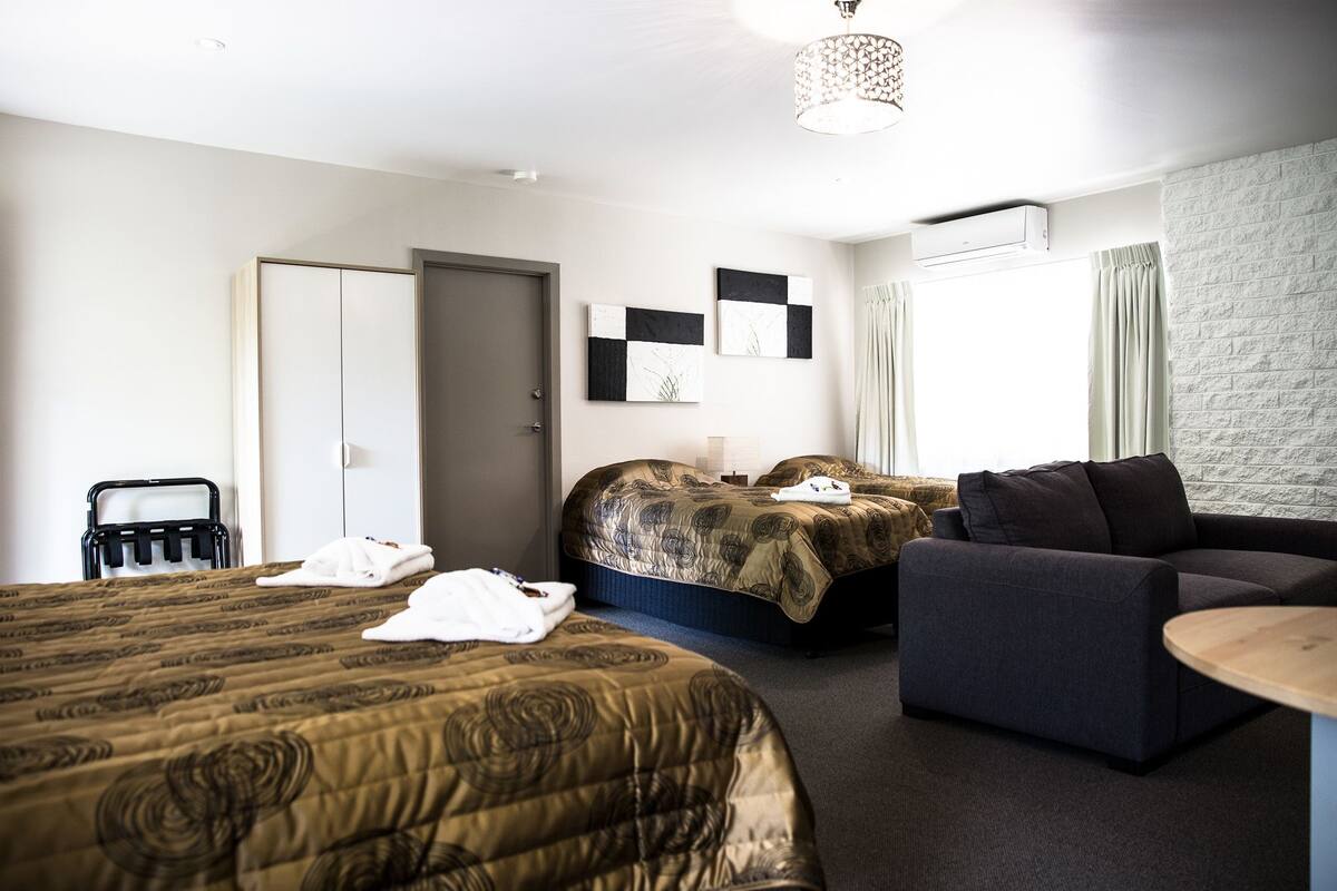 A hotel room with two beds, a sofa, a small table, and a shower area.