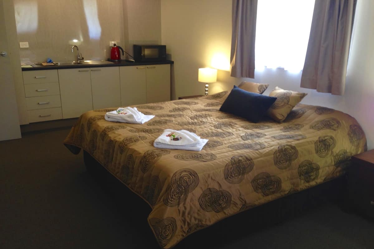 A hotel room with a bed, a desk with a microwave, a lamp, and a window with curtains.