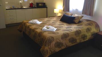 Habitación de hotel con cama, escritorio con microondas, lámpara y ventana con cortinas.