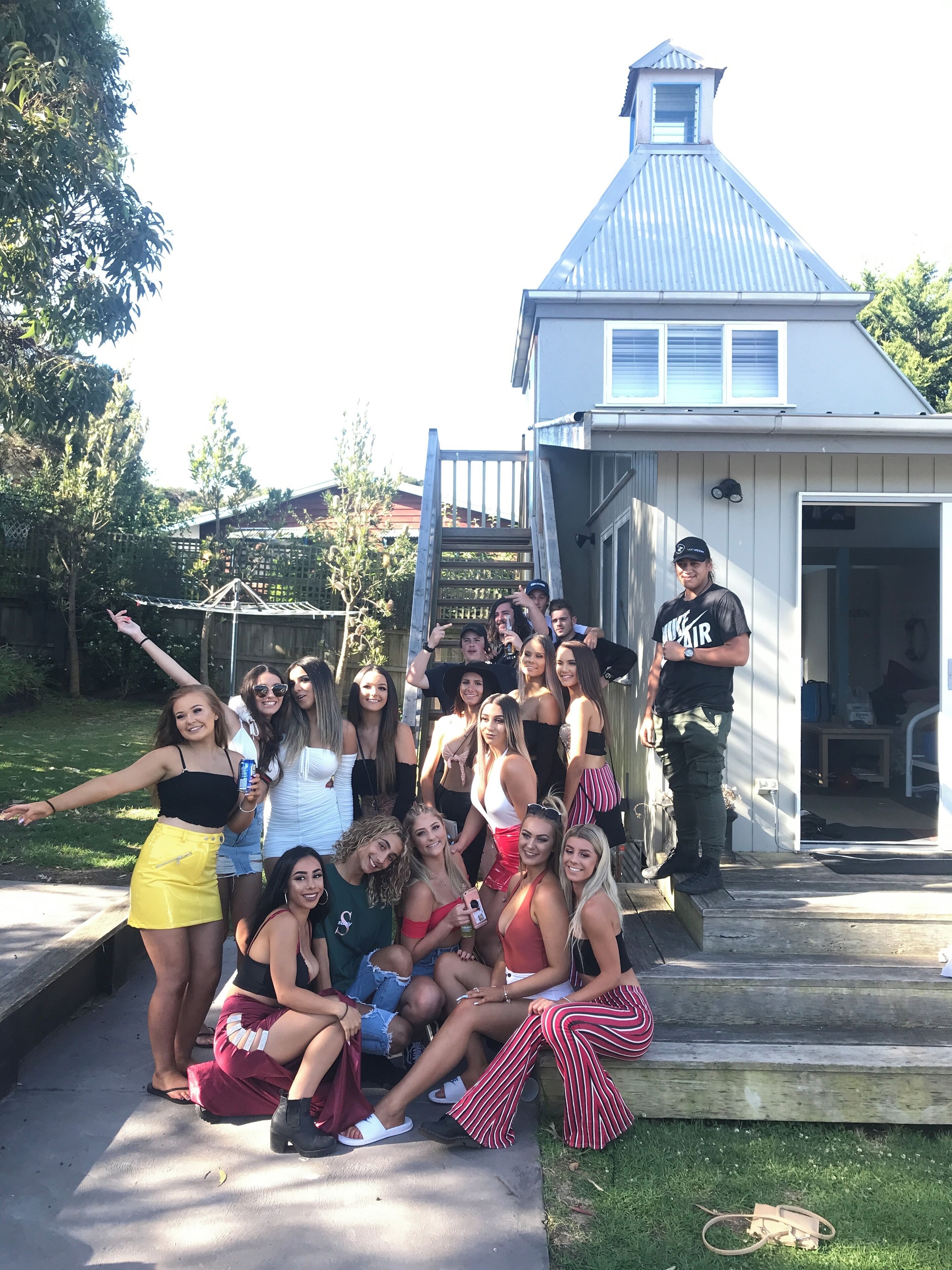 A group of people gathered outside a building with a sloped roof and a ladder leading to a deck.