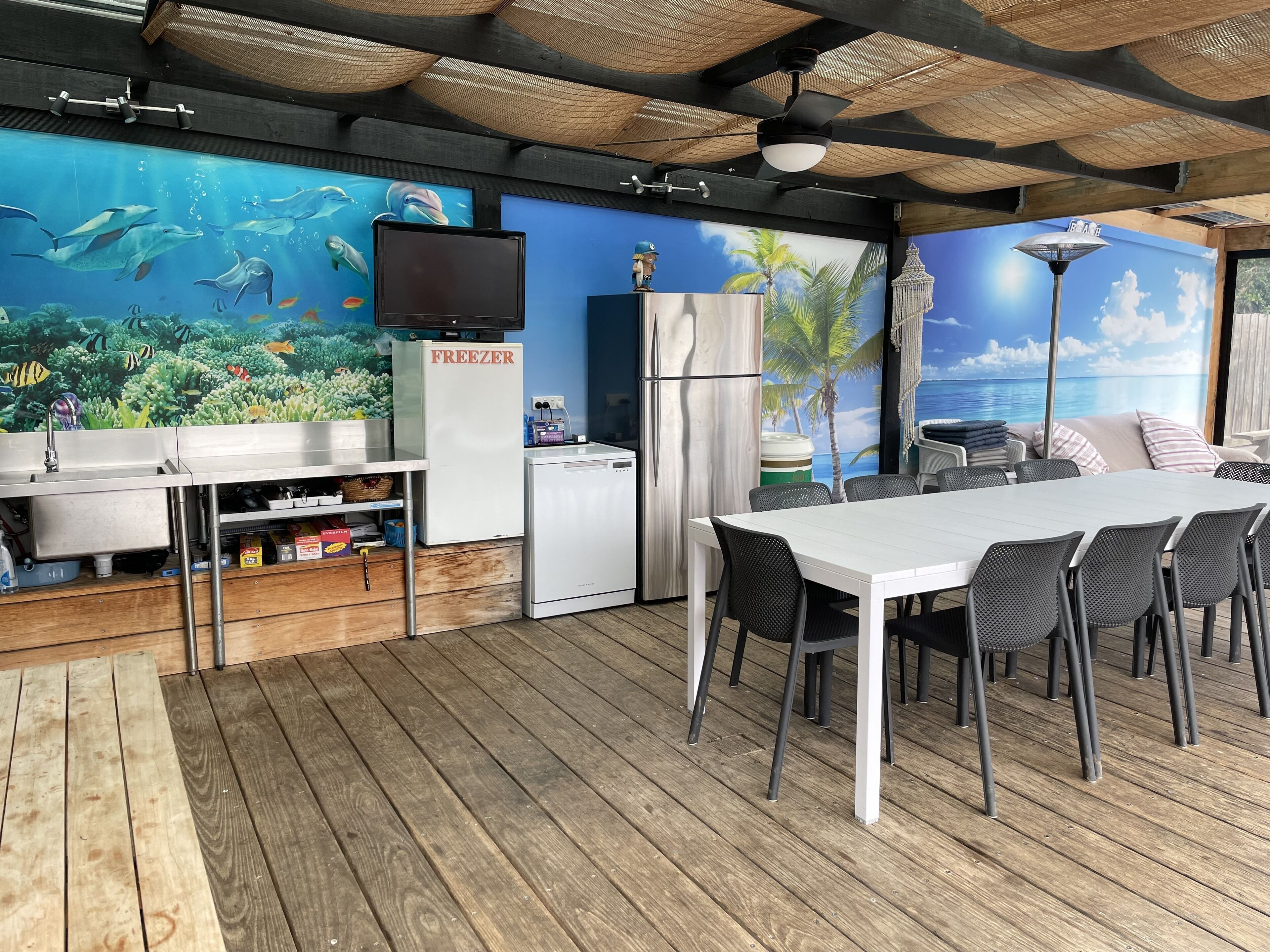 An outdoor kitchen area with a dining table and chairs, a refrigerator, and a freezer.