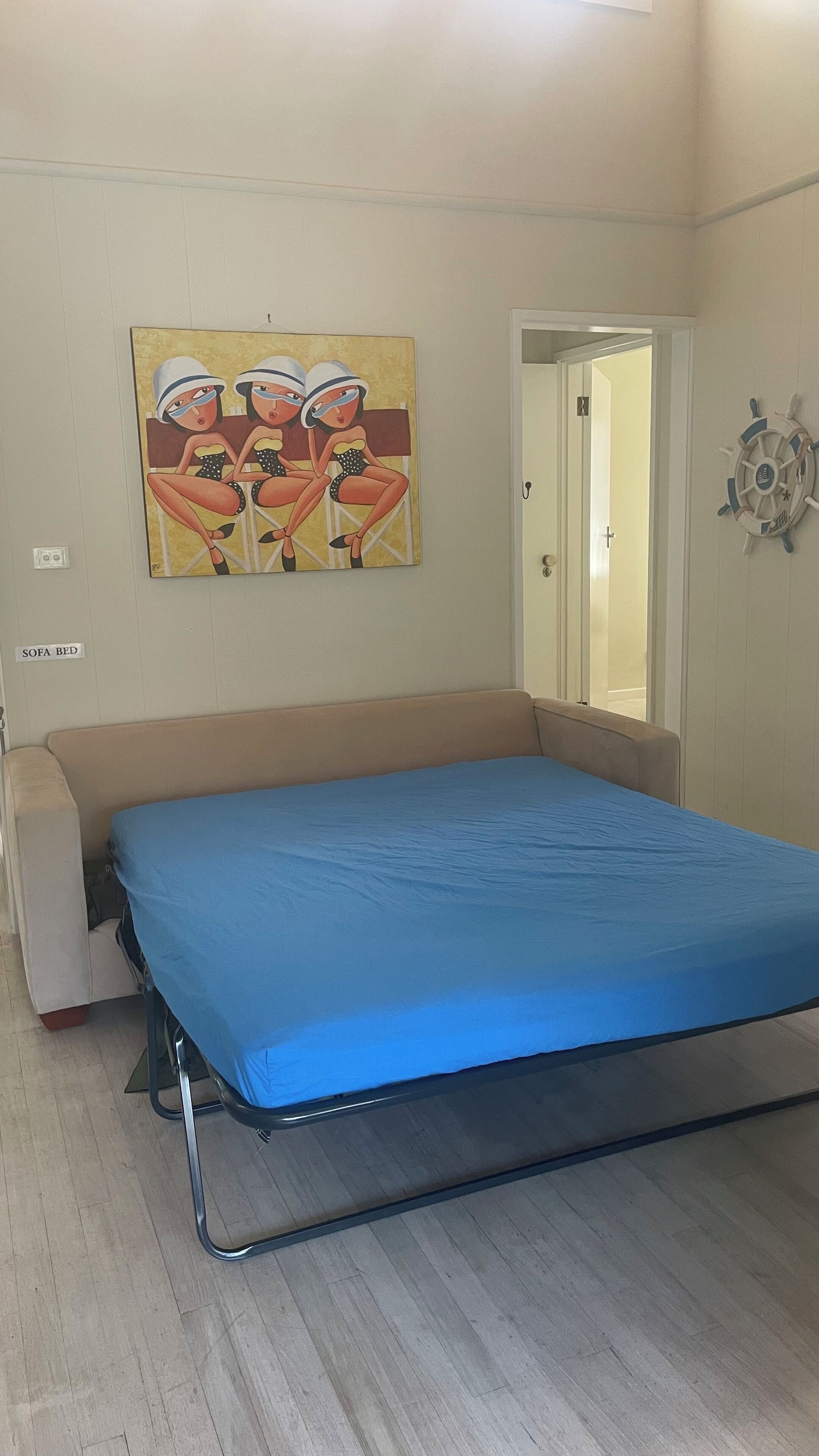 Una habitación con sofá cama, un cuadro en la pared y un adorno de timón.