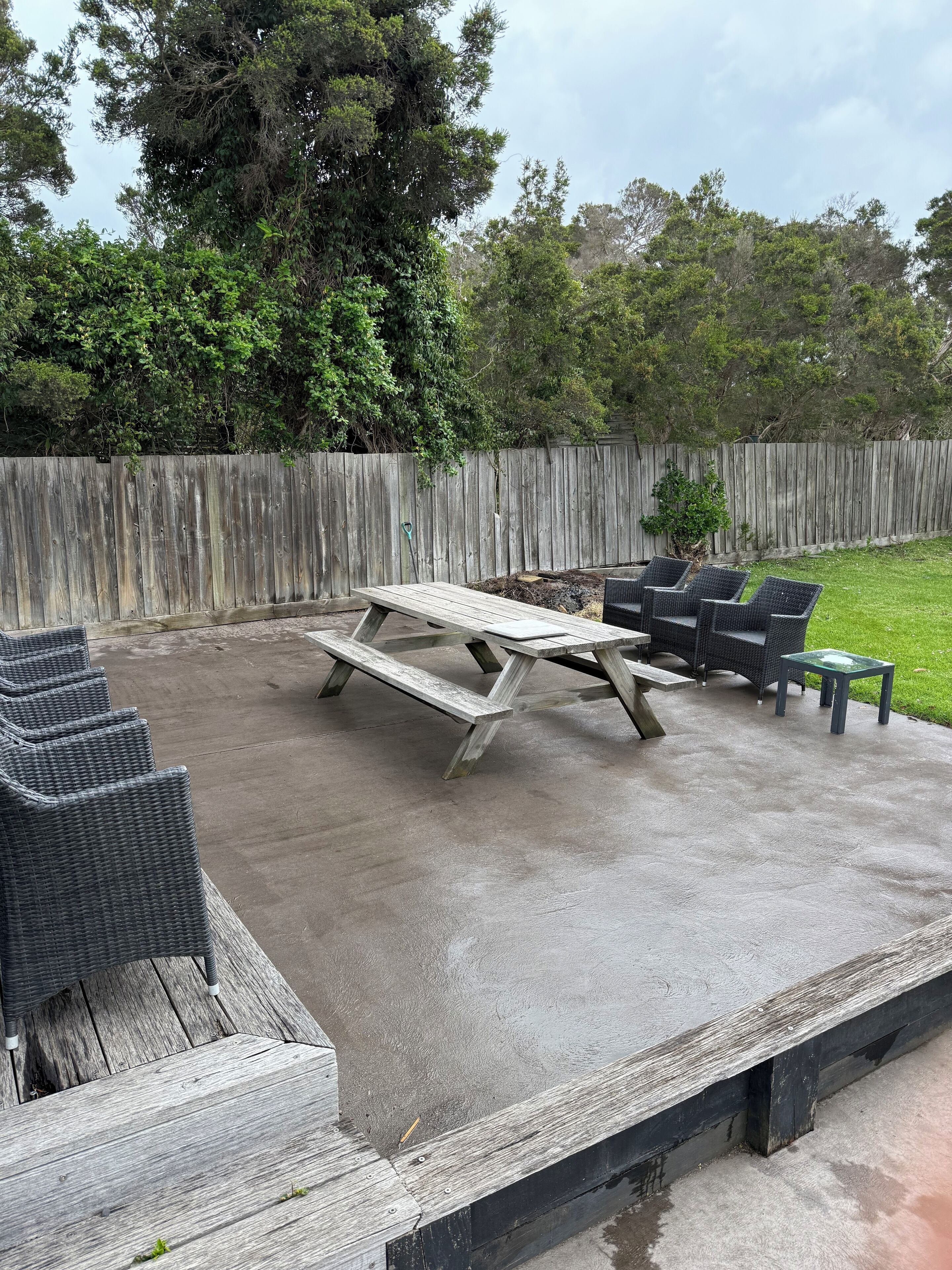 A concrete patio with a picnic table and wicker furniture.