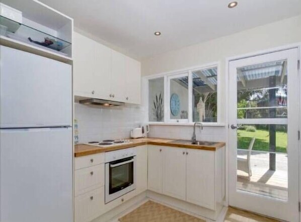 A kitchen with white cabinets, a built-in oven, a sink, and a window overlooking a garden.