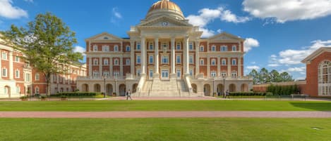A large, historic building with a central dome and symmetrical architecture, featuring multiple windows and a grand staircase leading to the entrance.
