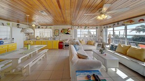 Amplia sala de estar con techo de madera, un ventanal con vistas y un comedor con armarios amarillos.