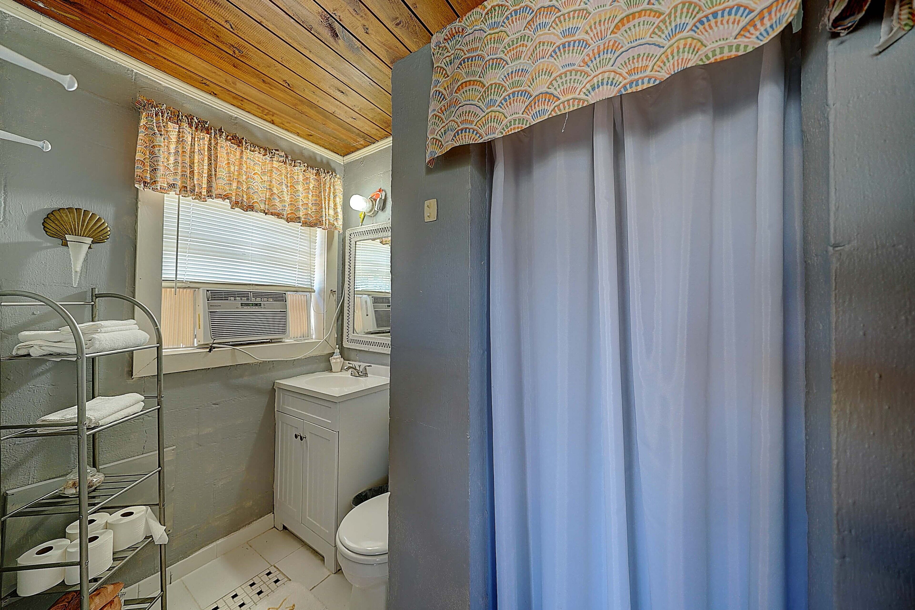 A bathroom with a wooden ceiling, a white sink, a toilet, and a shower curtain.