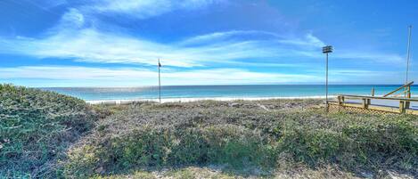 A beach with a wooden walkway leading to the water, a flagpole, and a clear sky.