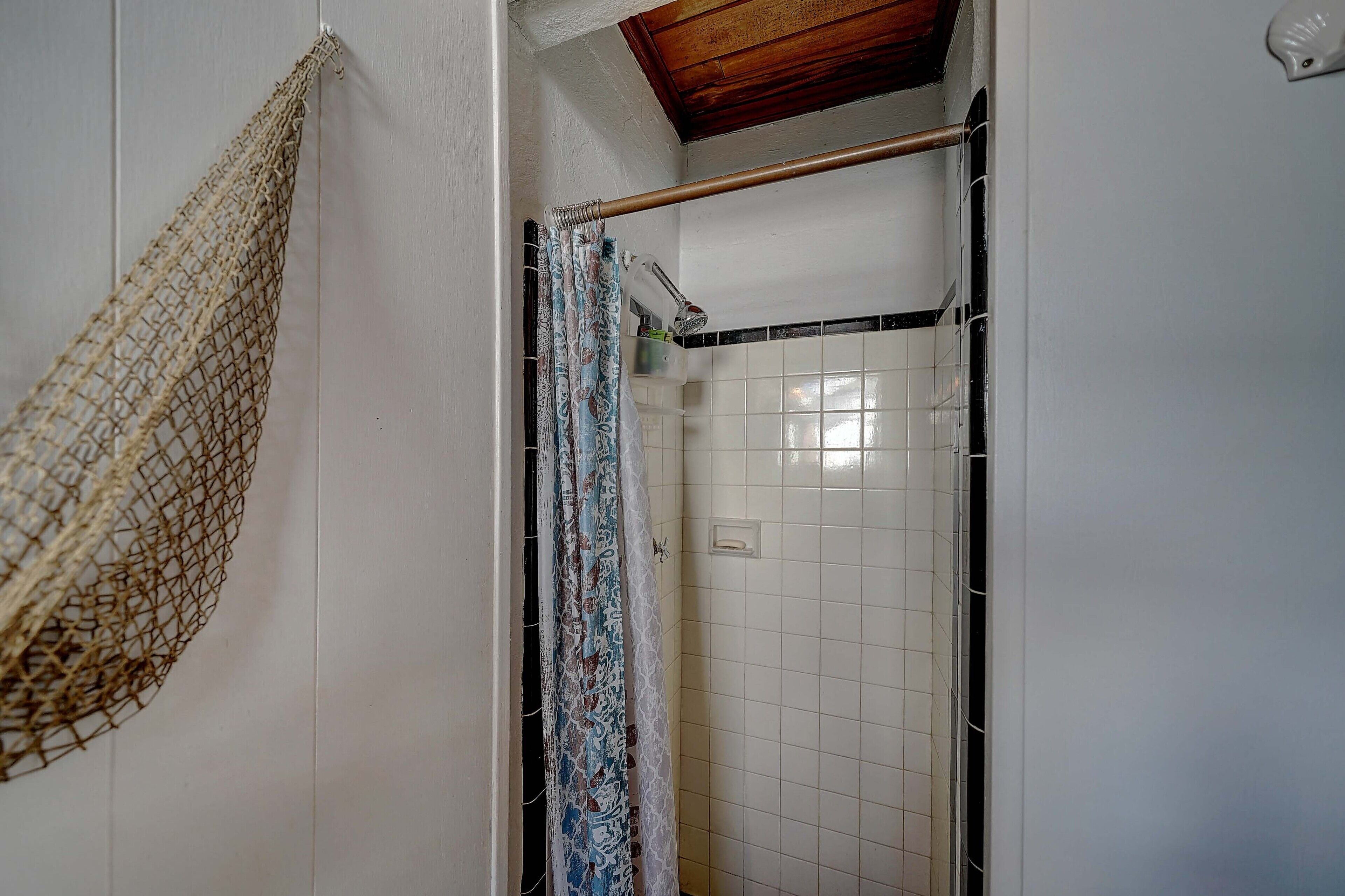 Een badkamer met douche, betegelde muren, een houten plafond en een hangend net.
