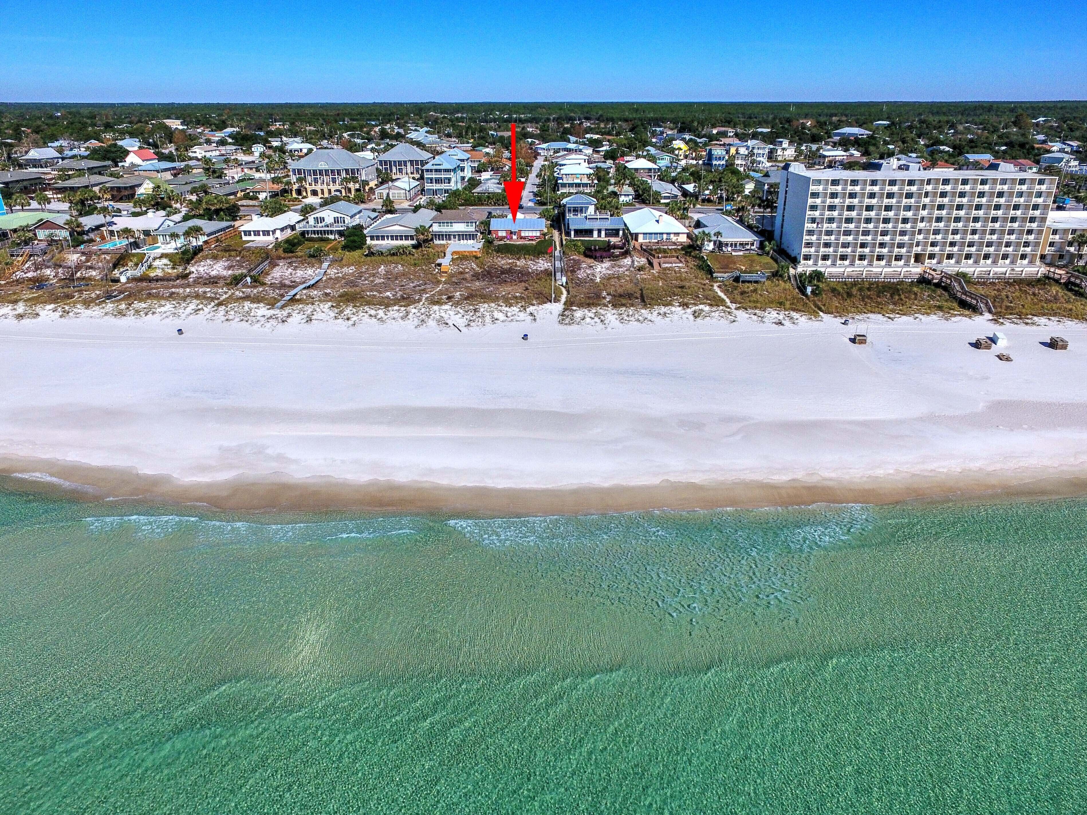 Luchtbeeld van een kustplaats met strandwoningen, een groot hotel en helder turquoise water.