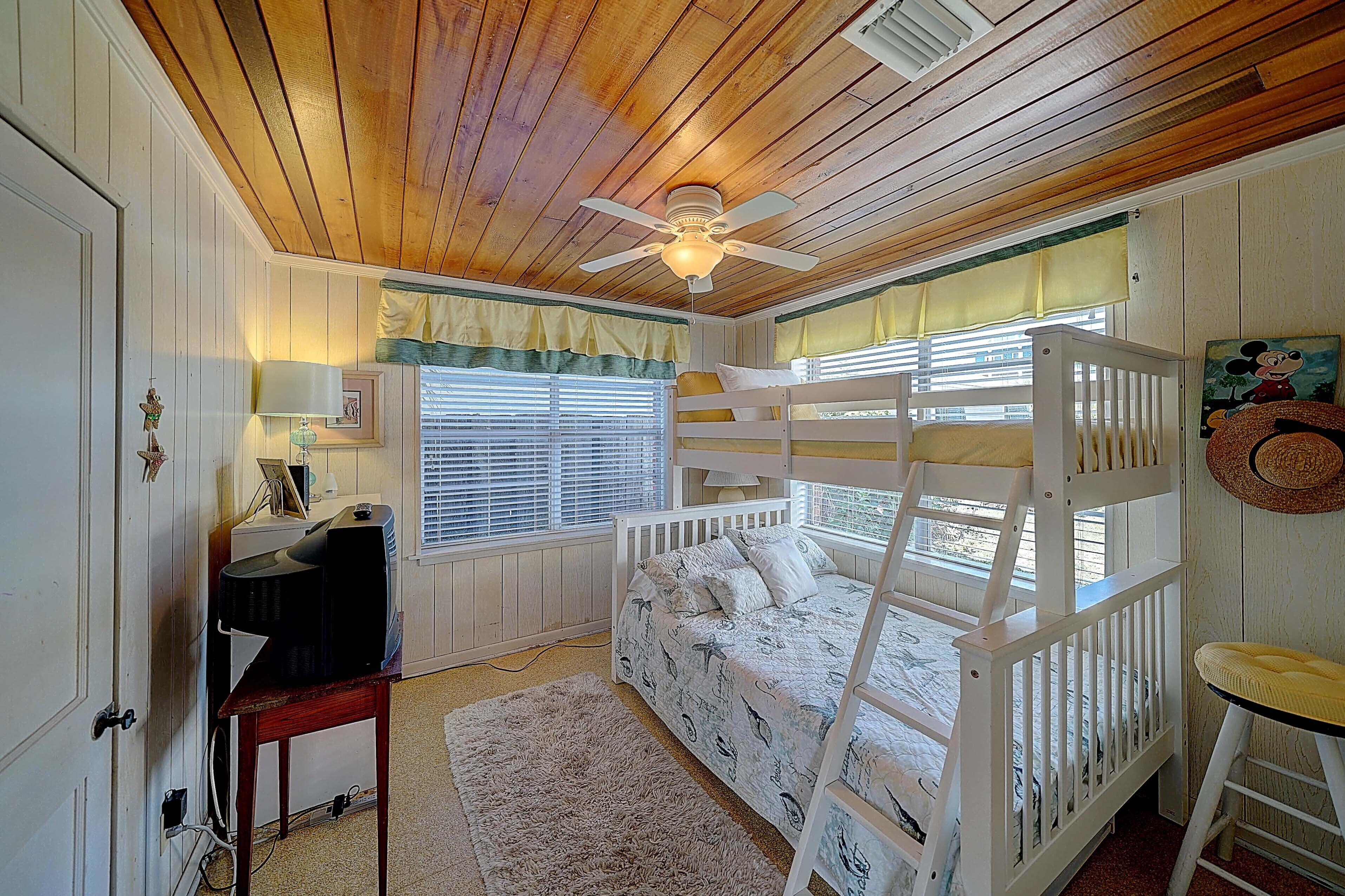 Une chambre avec un lit superposé, un bureau avec un ordinateur et un ventilateur de plafond.