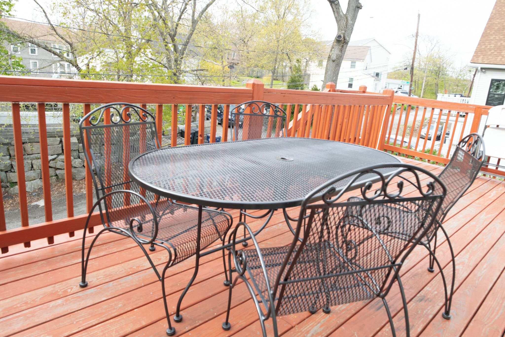 A round metal table with four chairs on a wooden deck with a red railing.
