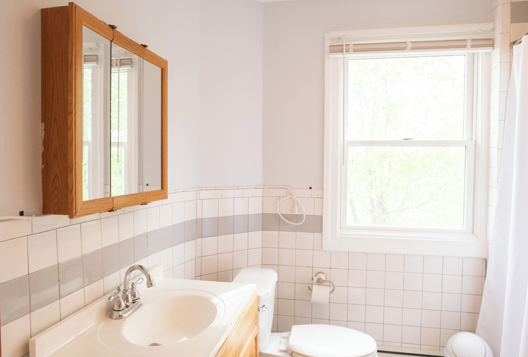 A bathroom with a white sink, a mirror, a toilet, and a window.