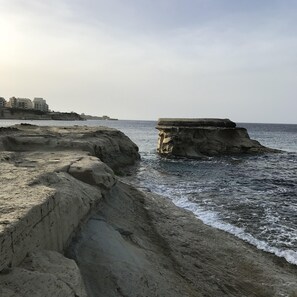 Paesaggio costiero con formazioni rocciose e una vista lontana di edifici.