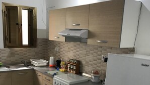 A compact kitchen with wooden cabinets, a built-in oven, a white refrigerator, and a tiled backsplash. - Cosy Air-conditioned Studio Marsalforn Beach (Marsalforn, Żebbuġ Gozo)