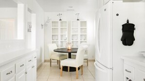 A modern kitchen with white cabinetry, a round dining table with chairs, and a built-in shelving unit with glass doors.