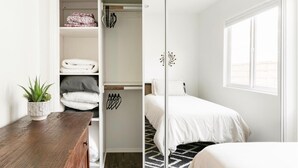 A bedroom with a bed, a wardrobe, a bedside table with a plant, and a window.