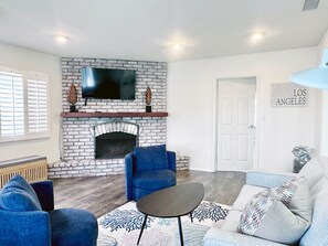 A living room with a brick fireplace, a flat-screen TV, blue sofas, and a 'Los Angeles' sign.