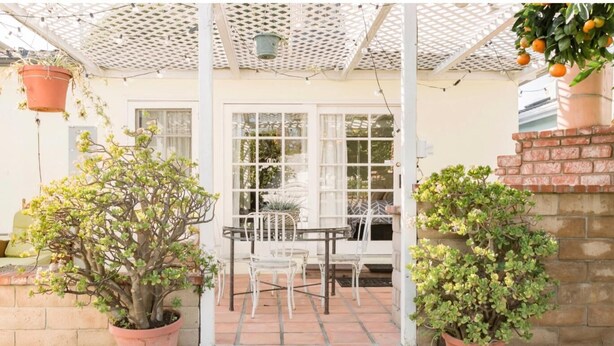 A patio area with a table and chairs, surrounded by potted plants and a white fence.