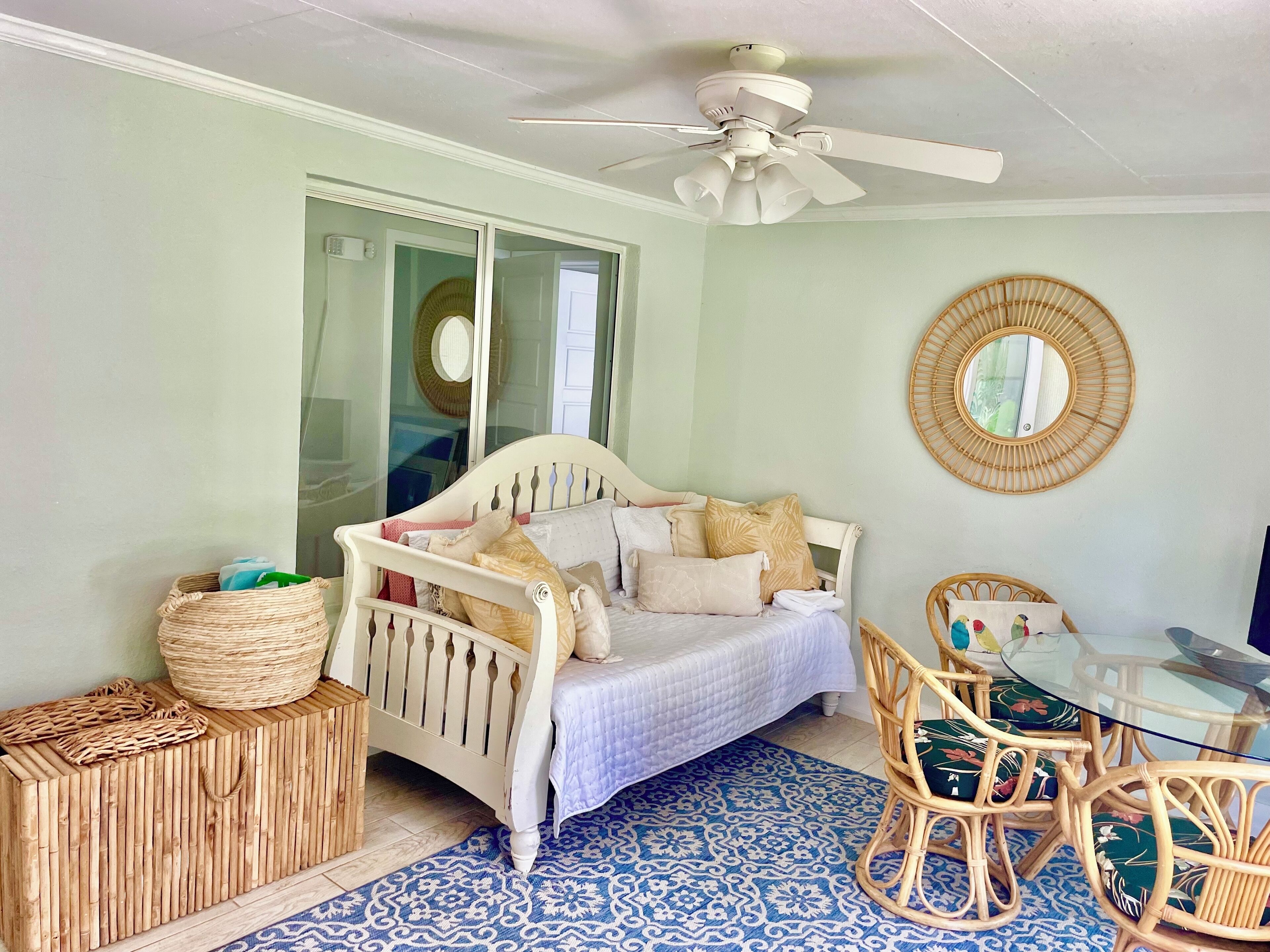 A bedroom with a bed, a ceiling fan, a round mirror, wicker furniture, and a patterned rug.