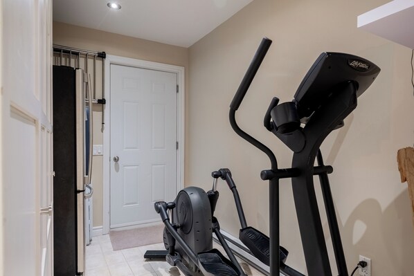 Un gimnasio en casa con equipo de ejercicio, una puerta y una lámpara fijada a la pared.