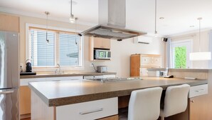 Una cocina moderna con una isla central, electrodomésticos de acero inoxidable y un amplio ventanal con persianas.