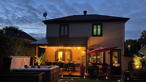 A two-story house with a patio area featuring outdoor seating and string lights.