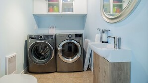 A compact laundry room with two front-loading washing machines, a sink, and a mirror.