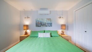 A bedroom with a green quilted bedspread, two bedside lamps, a painting on the wall, and a white door.