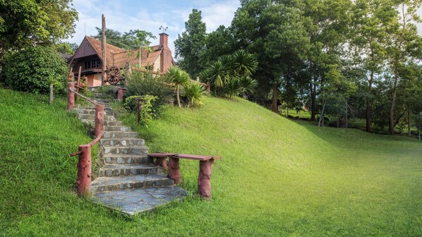 Una escalera de piedra que conduce a una casa con techo rojo, rodeada de abundante follaje y árboles.