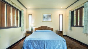 A bedroom with a wooden bed, two bedside tables, a nightstand, a window with curtains, and a wall-mounted painting. - Khao Kho Valley Hotel (Khao Kho)