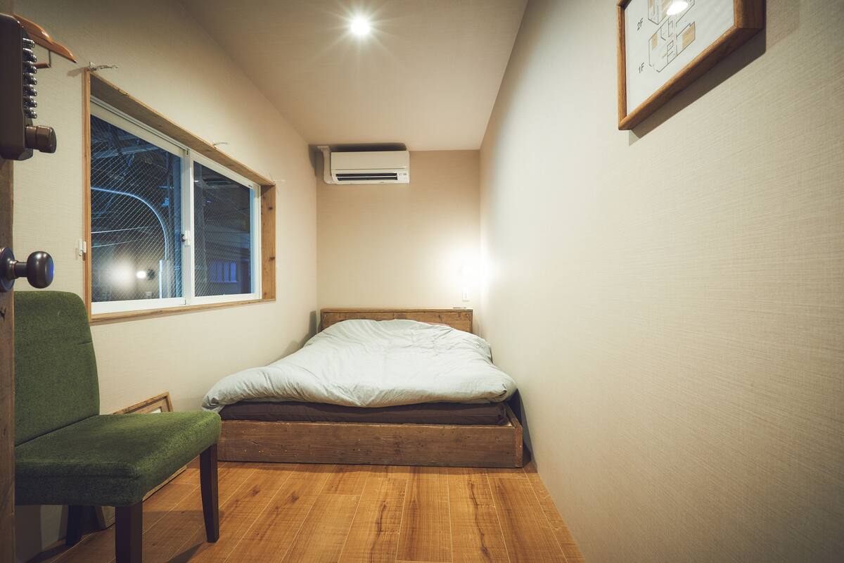 Un dormitorio pequeño y acogedor con una cama de madera, una silla verde y una ventana con persianas.